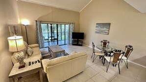 A living room with a sofa, coffee table, TV, and dining table with chairs. - Bright and cheery Gold-rated condo with excellent lagoon views! (Saint Augustine)