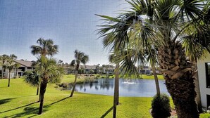 A well-maintained lawn with palm trees, a pond, and a building in the background. - Bright and cheery Gold-rated condo with excellent lagoon views! (Saint Augustine)
