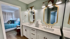 Un baño con tocador doble, un espejo grande con detalles dorados y una cama visible en la habitación contigua.