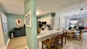 Una cocina moderna con armarios blancos, una isla central y una zona de comedor con sillas de mimbre.