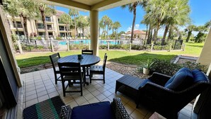 Un patio techado con vista a la piscina, mobiliario exterior y vista del edificio del hotel.