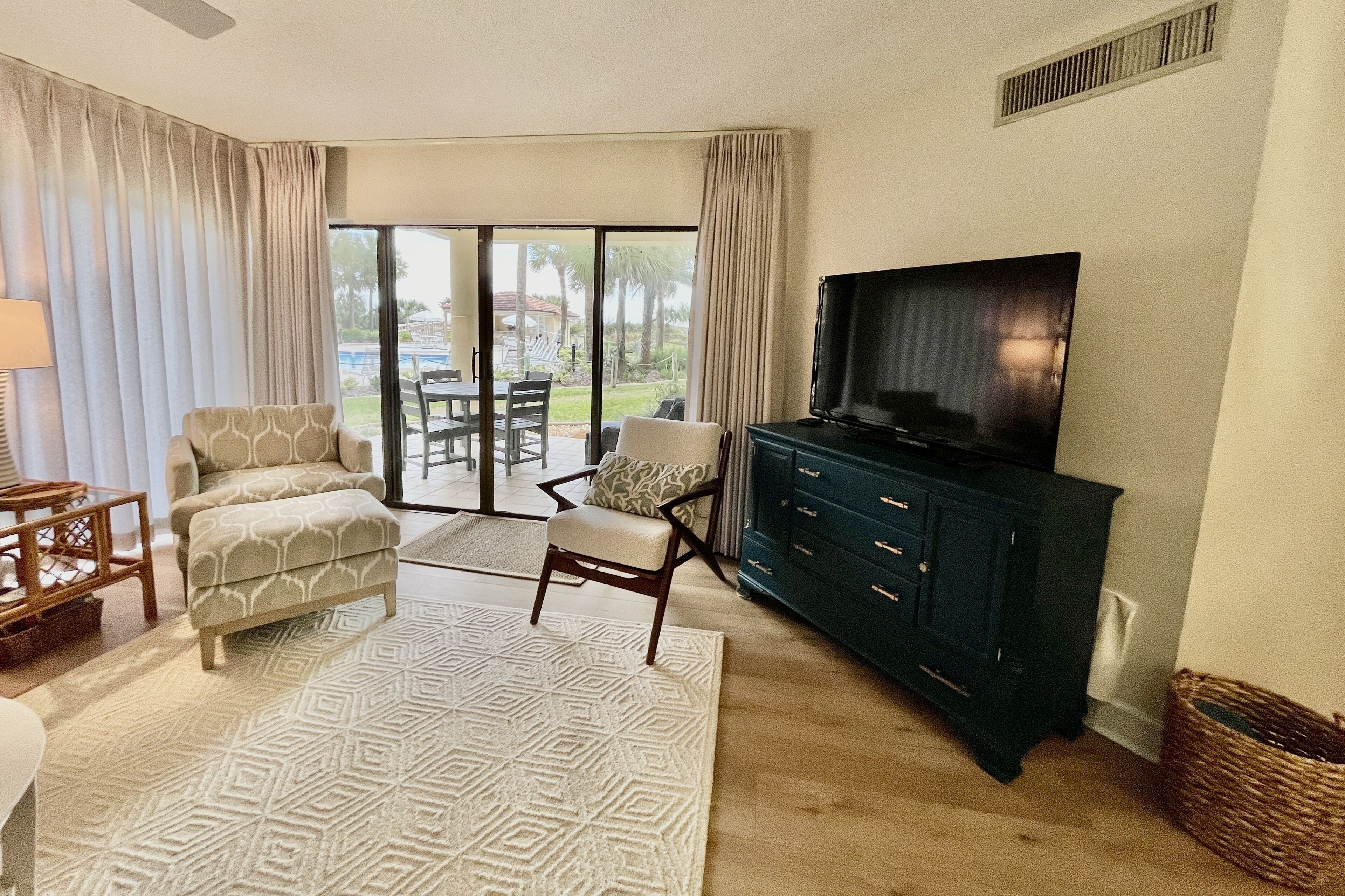 A living room with a sofa, armchair, and TV stand. There is a sliding glass door leading to an outdoor area.