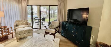 A living room with a sofa, armchair, and TV stand. There is a sliding glass door leading to an outdoor area.