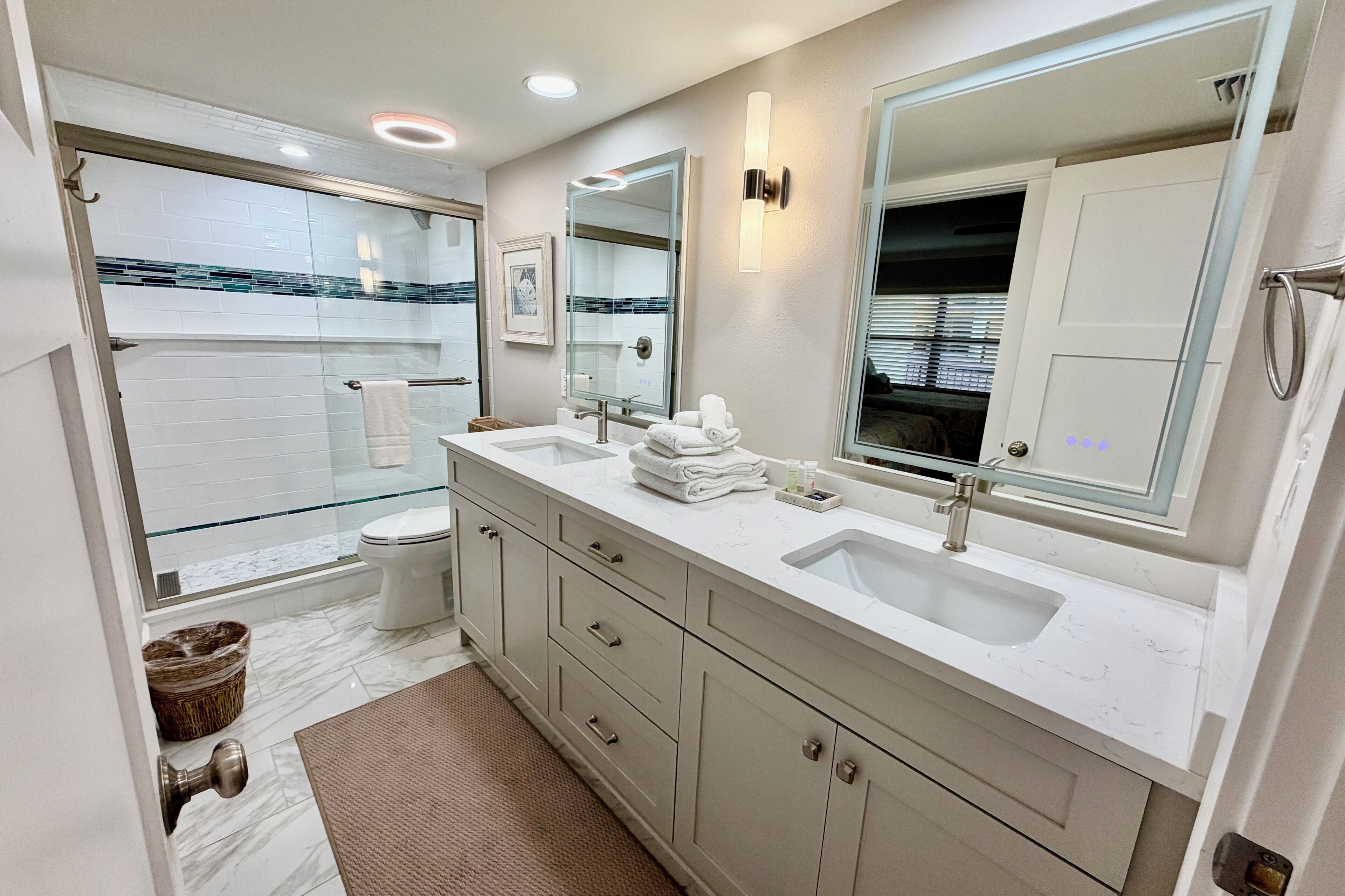 A modern bathroom with a double sink vanity, a large mirror, and a glass shower enclosure.