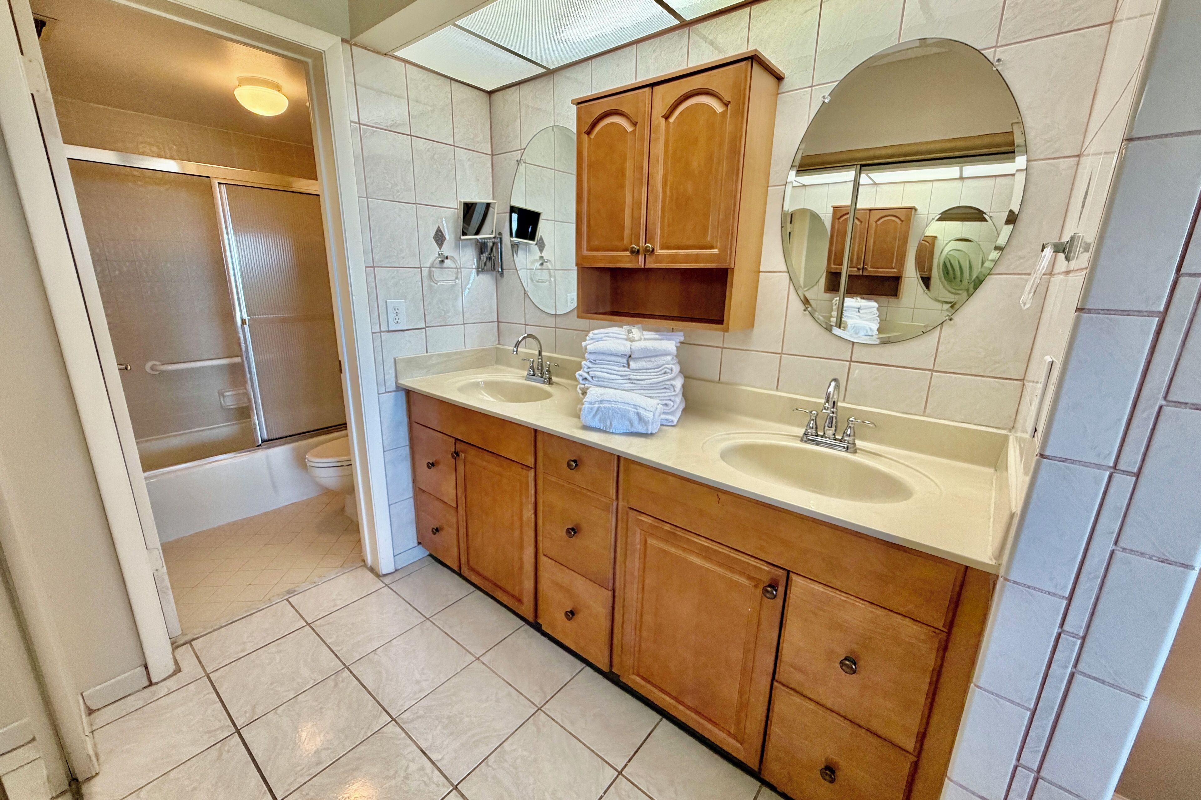 A bathroom with two sinks, wooden cabinets, a mirror, and a shower.