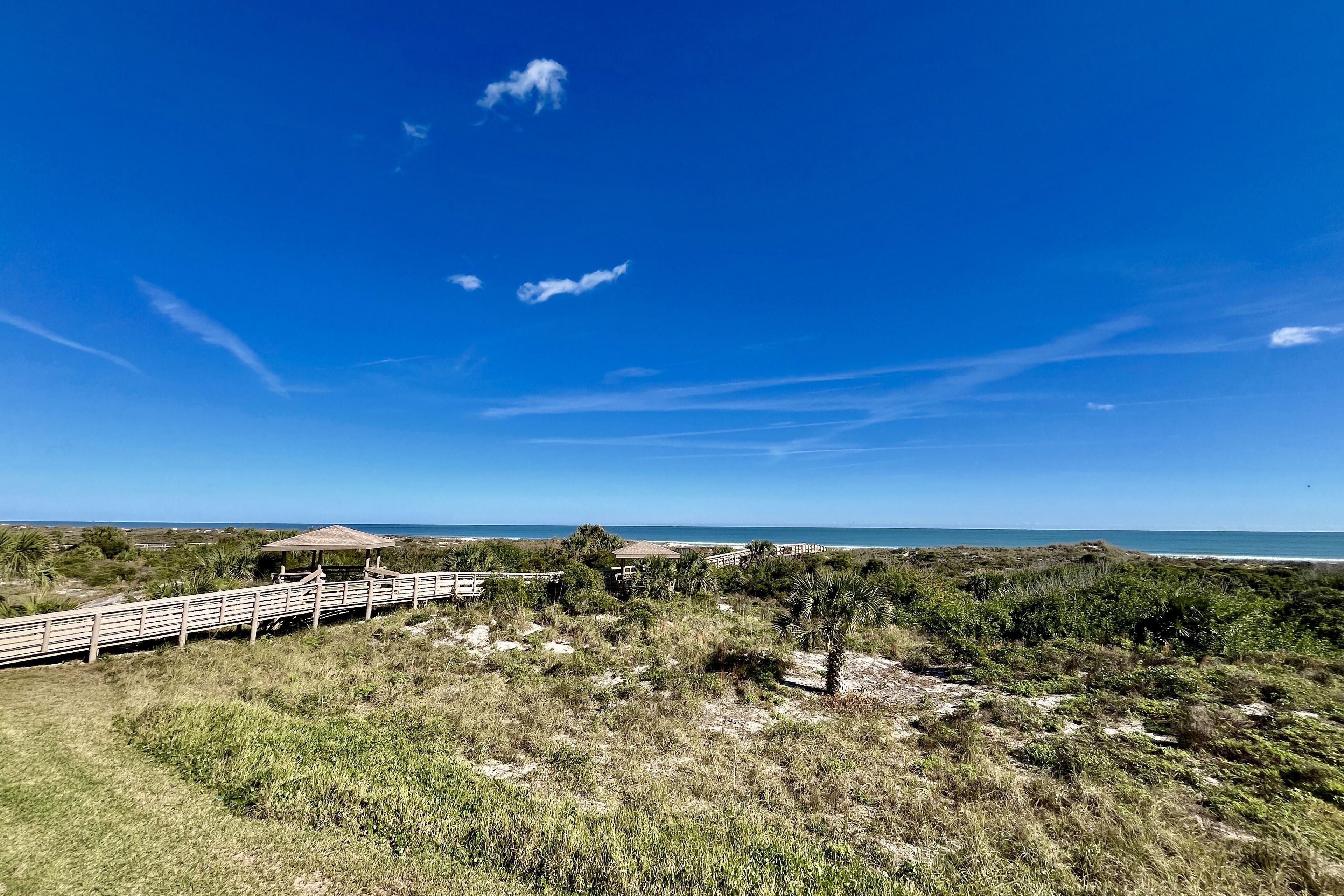 Un paysage côtier avec une promenade en bois, des cabanes de plage et une vue dégagée sur l’océan.