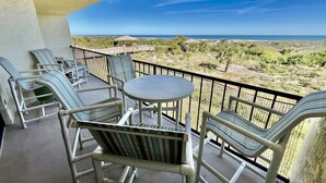 En balkon med fletstole og et bord, med udsigt over en strand og et tørt landskab.