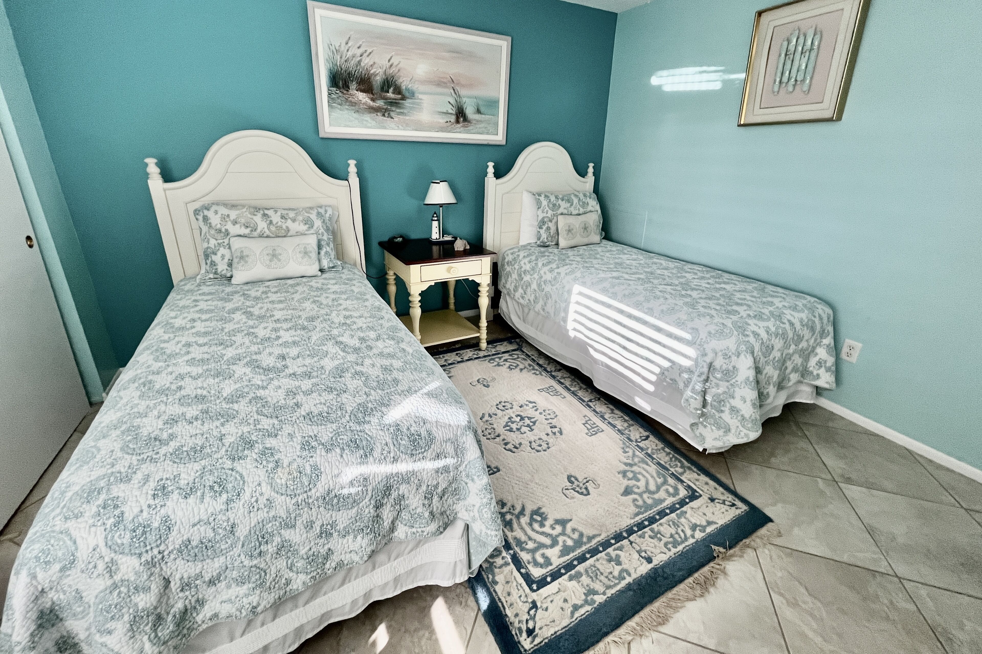 A room with two beds, a nightstand, a lamp, and a rug.