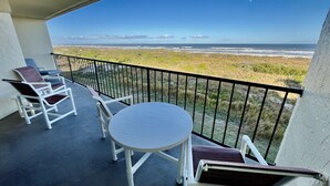 A balcony with a table and chairs, overlooking a beach and ocean. - ENJOY FREE FUN EVERYDAY and a Cheerful ocean front condo with stunning view of the ocean. (Saint Augustine)