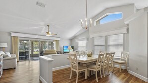 A spacious living room with a large wooden dining table, a sofa, and a TV. - Enjoy your beach vacation in this Gold-rated single family home! (Saint Augustine)
