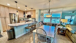 Una cocina con una isla central, armarios de madera, electrodomésticos de acero inoxidable y una zona de comedor con sillas y una mesa.