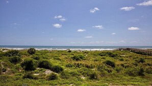A coastal landscape with a wooden boardwalk leading to the beach, surrounded by dense green vegetation. - FREE FUN DAILY with this beautiful corner unit with substantial wrap around porch and marvelous views of the Atlantic Ocean! (St. Augustine)