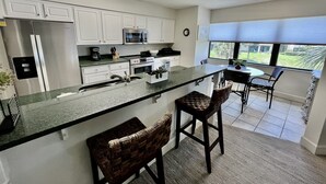 A modern kitchen with white cabinets, stainless steel appliances, a granite countertop, and a dining area with a view. - FREE FUN DAILY with this beautiful corner unit with substantial wrap around porch and marvelous views of the Atlantic Ocean! (St. Augustine)