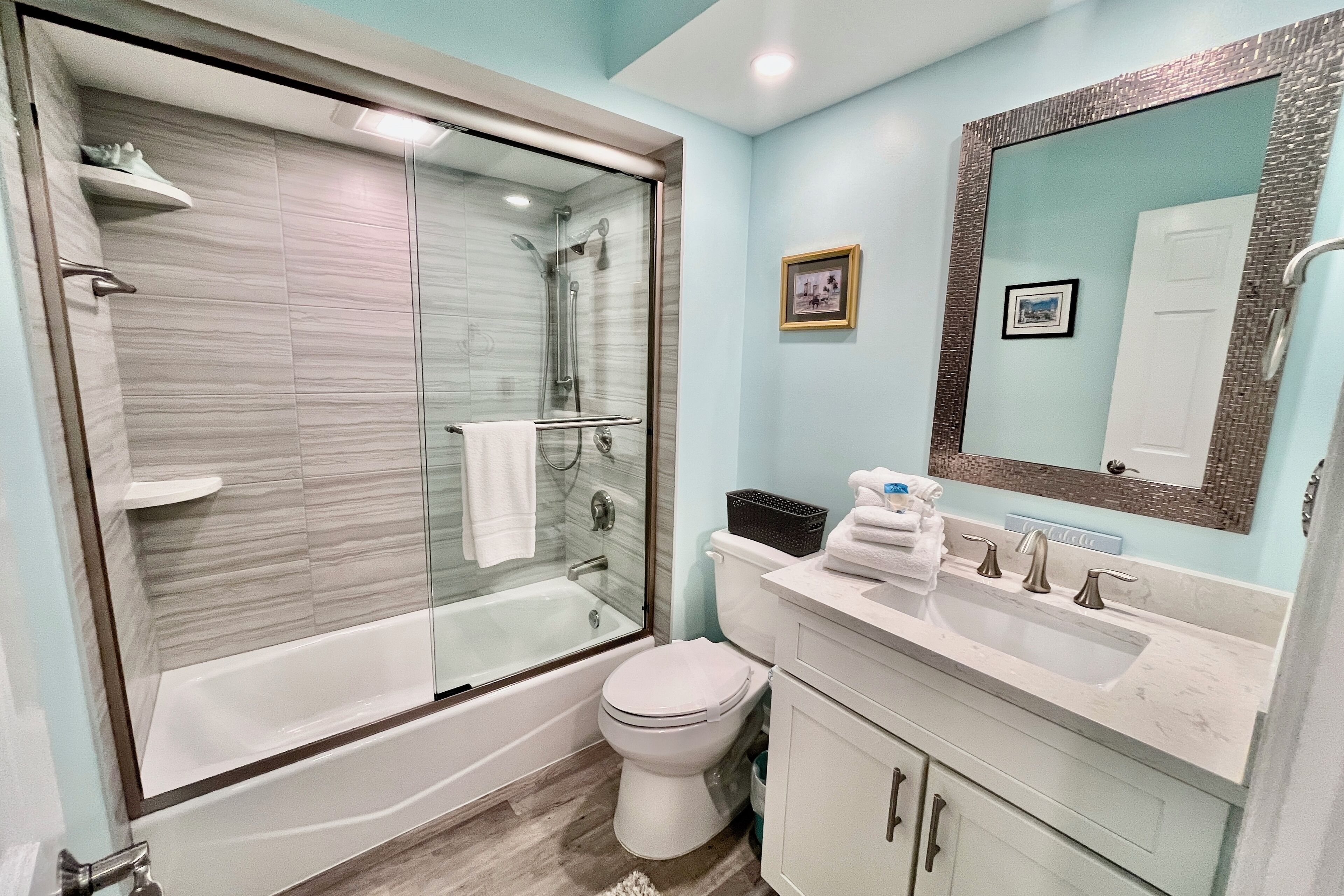 A modern bathroom with a glass-enclosed shower, a white toilet, a sink with a mirror, and a light blue wall.