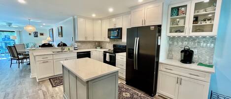 A modern kitchen with white cabinetry, a central island, stainless steel appliances, and a dining area with a view.