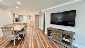 Un comedor amplio con una mesa y sillas de madera, un televisor fijado a la pared y un aparador con libros.
