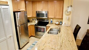 A kitchen with wooden cabinets, stainless steel appliances, a marble countertop, and a sink. - Enjoy your morning coffee on your covered lanai, then head over to beach only a brisk walk away! (Saint Augustine)