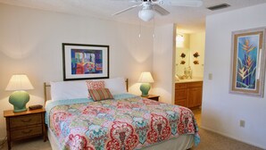 Un dormitorio con una cama grande, dos mesitas de noche con lámparas, un ventilador de techo y obras de arte en las paredes.