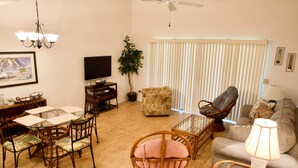 A living room with a dining table, chairs, a sofa, a TV, and a ceiling fan. - Enjoy your morning coffee on your covered lanai, then head over to beach only a brisk walk away! (Saint Augustine)