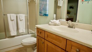 Un baño con bañera, inodoro y tocador con lavabo y espejo.