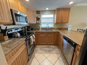 A compact kitchen with wooden cabinets, a stainless steel stove, a dishwasher, and a granite countertop. - Pelican Cove 9 - Anna Maria Island - Condo 2 Bedroom /2 Bath bay side, maximum occupancy of 5 people. (Bradenton Beach)