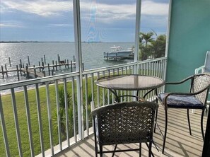A balcony with a view of the water, a round table, and two wicker chairs. - Pelican Cove 9 - Anna Maria Island - Condo 2 Bedroom /2 Bath bay side, maximum occupancy of 5 people. (Bradenton Beach)