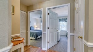 Ein Flur, der in ein Schlafzimmer mit Bett, Nachttisch und einem mit Vorhängen drapierten Fenster führt.