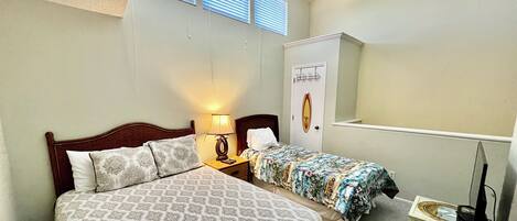 A bedroom with a large bed, two bedside tables, a ceiling fan, a nightstand with a lamp, a dresser, and a TV stand.