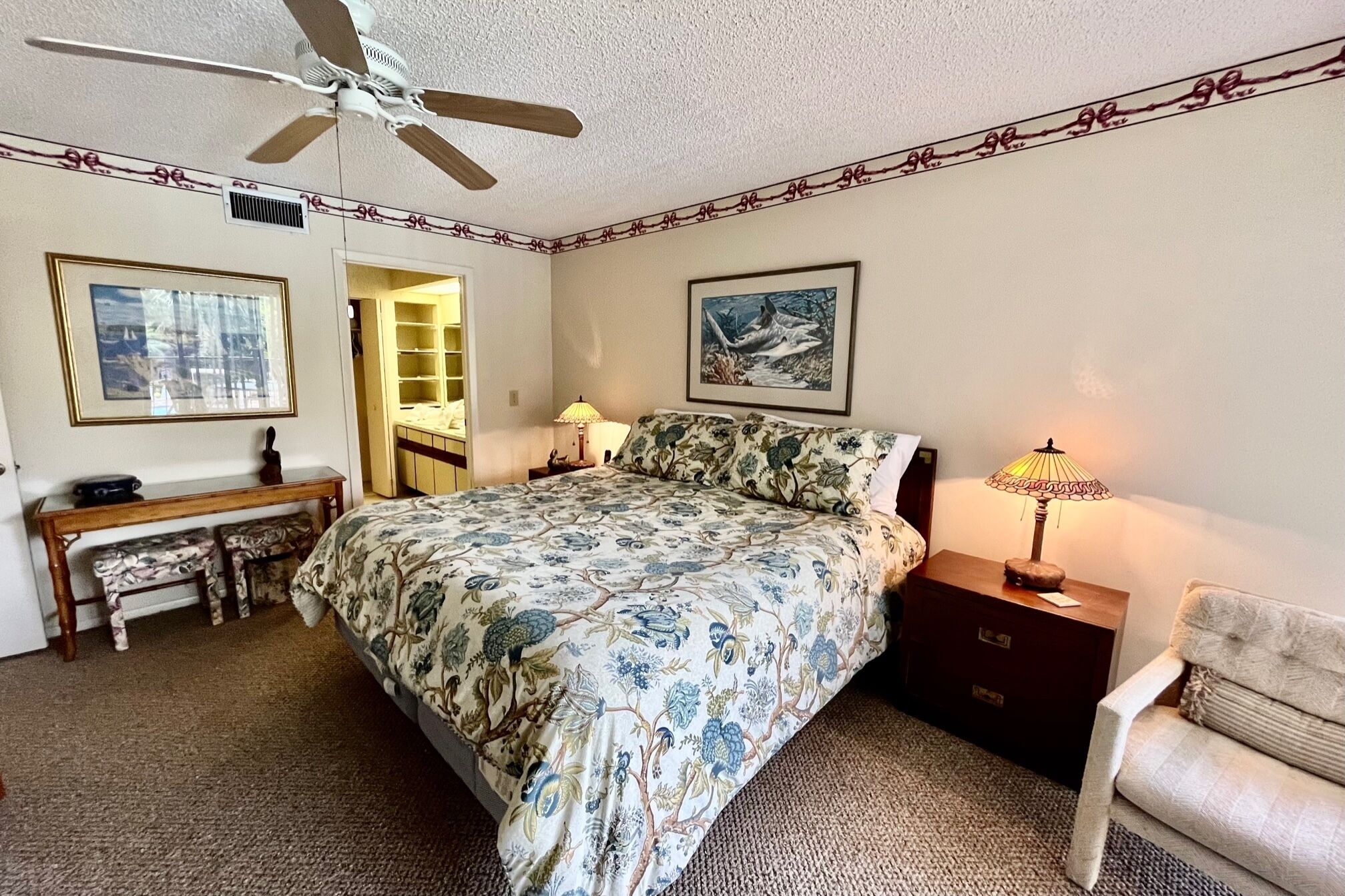A bedroom with a bed, a desk, a chair, a nightstand, a lamp, a ceiling fan, and a door leading to a closet.