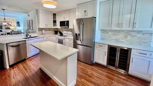 Une cuisine moderne avec des meubles blancs, des appareils électroménagers en acier inoxydable et un plancher en bois.
