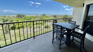 Un balcon avec une table et des chaises, offrant une vue sur un paysage côtier verdoyant et l’océan.