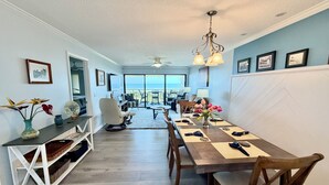 Un comedor con vista al océano, un ventilador de techo y una mesa con individuales y cubiertos.