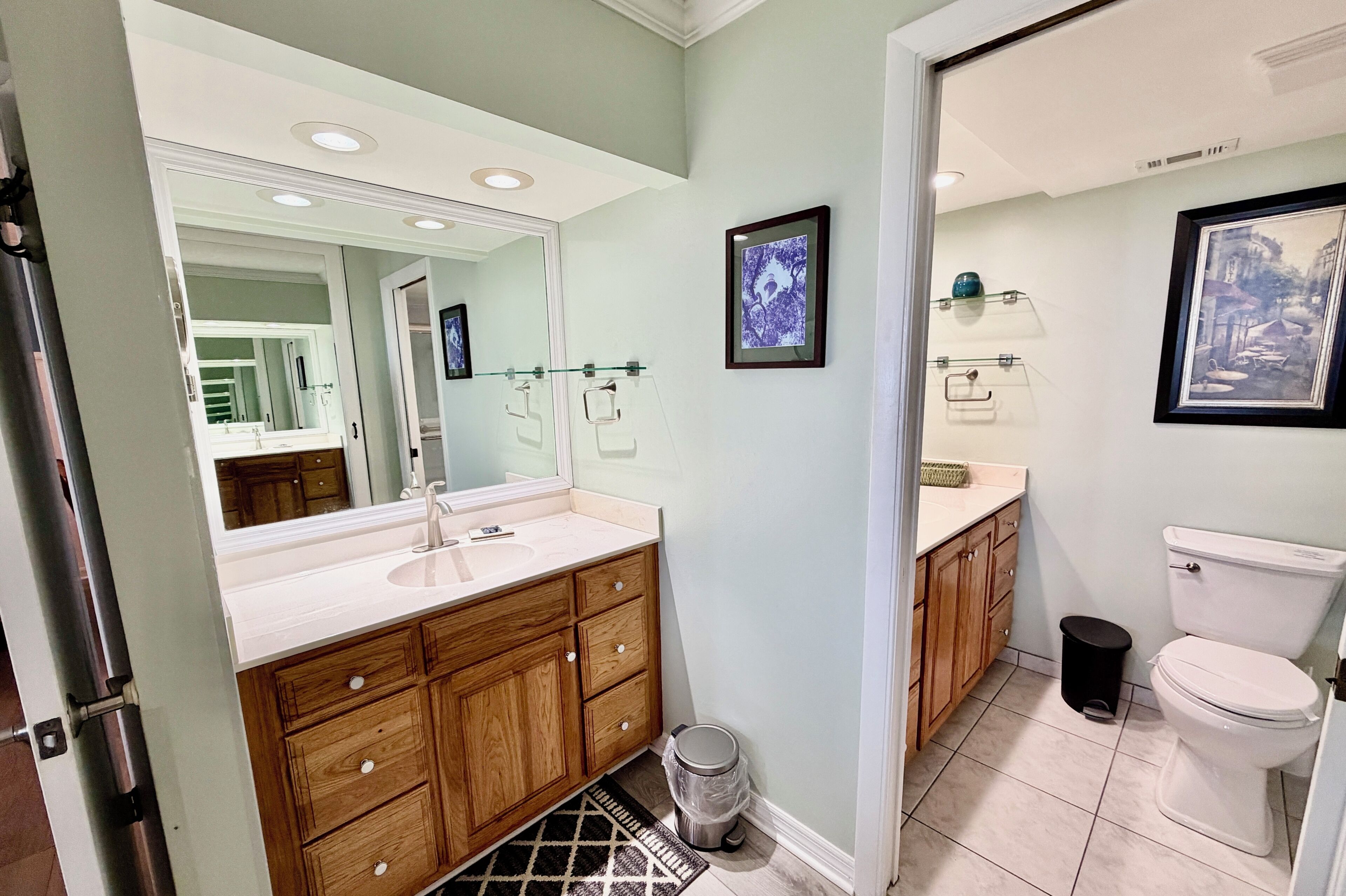 Une salle de bain avec un lavabo blanc, un meuble-lavabo en bois, un grand miroir, un tableau encadré au mur et des toilettes.