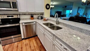 A modern kitchen with stainless steel appliances, white cabinetry, and a granite countertop. - Spacious ocean front condo, perfect for sipping your morning coffee and enjoying the gentle waves! (Saint Augustine)