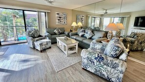 A spacious living room with a large window, a ceiling fan, and a flat-screen TV. - Comfortable Gold-rated condo perfect for the best vacation yet! (Saint Augustine)