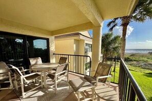 Un balcon avec une table et des chaises, une vue sur l’océan et un palmier.