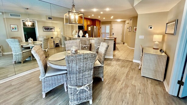 A dining area with wicker furniture, a chandelier, and a kitchen in the background. - Comfortable Gold-rated condo perfect for the best vacation yet! (Saint Augustine)