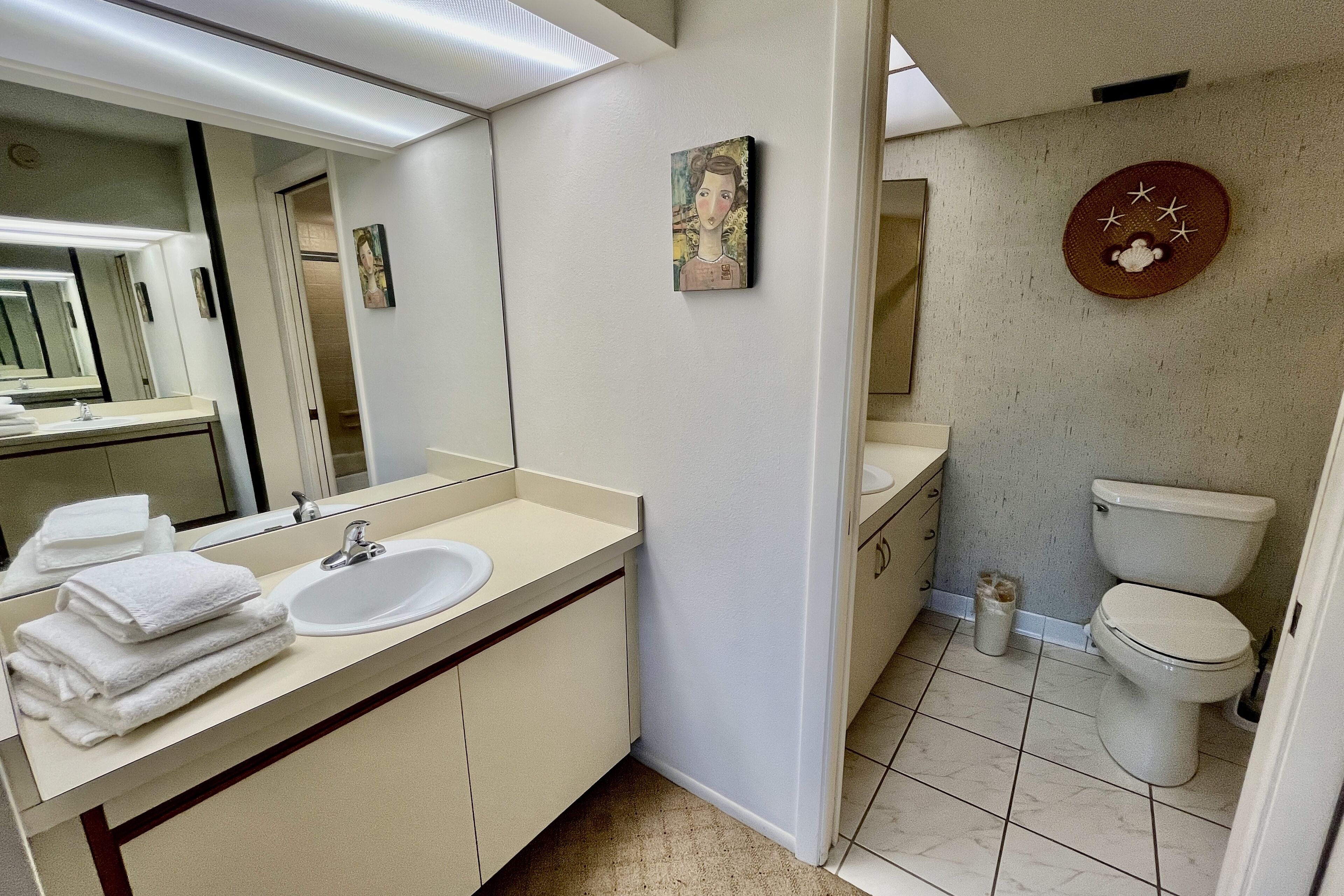 Une salle de bain avec un lavabo, un miroir et des toilettes. Des serviettes sont pliées et empilées sur le comptoir.