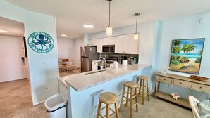 Una cocina moderna con una isla central, taburetes de bar, un refrigerador y un microondas.