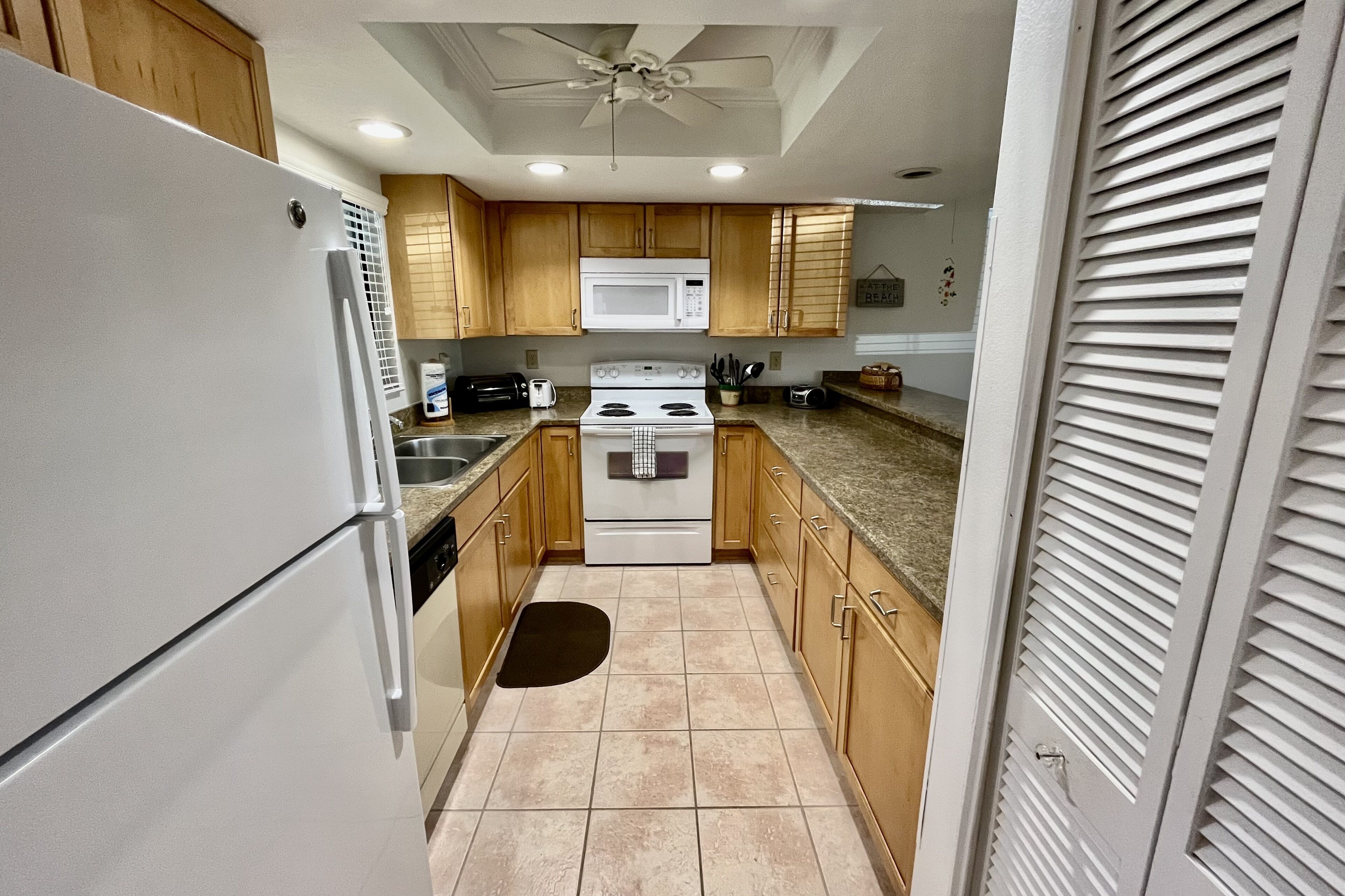 A kitchen with wooden cabinets, a white refrigerator, a microwave, a stove, and a ceiling fan.