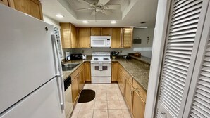 Une cuisine avec des meubles de rangement en bois, un réfrigérateur blanc, un four à micro-ondes, une cuisinière et un ventilateur de plafond.