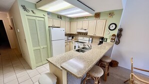 Eine kleine Küche mit Kühlschrank, Herd, Spüle und Barhocker.