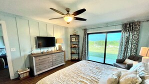 Un dormitorio con una cama grande, un ventilador de techo, un televisor, un aparador y vistas al exterior a través de una puerta corrediza de vidrio.