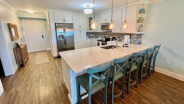 Una cocina moderna con armarios blancos, una isla grande, taburetes de bar e iluminación colgante.