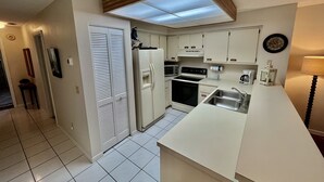 Une cuisine compacte avec des meubles blancs, un four encastré, un four à micro-ondes et un évier.