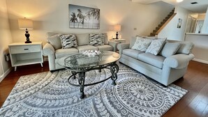 A living room with a beige sofa, a glass coffee table, patterned rugs, and two lamps. - Comfortable condo with easy beach and pool access! (Saint Augustine)