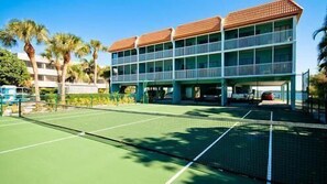 A tennis court with a net, adjacent to a multi-story building with balconies. - Pelican Cove 10 - Anna Maria Island - Condo 2 Bedroom /2 Bath bay view,  maximum occupancy of 5 people. (Bradenton Beach)
