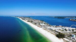 An aerial view of a coastal town with a long sandy beach, clear blue waters, and a mix of residential and commercial buildings. - Gulf Watch 216 - Anna Maria Island - Condo 2 Bedroom / 2 Bath Gulf to Bay access, maximum occupancy of 4 people . (Bradenton Beach)