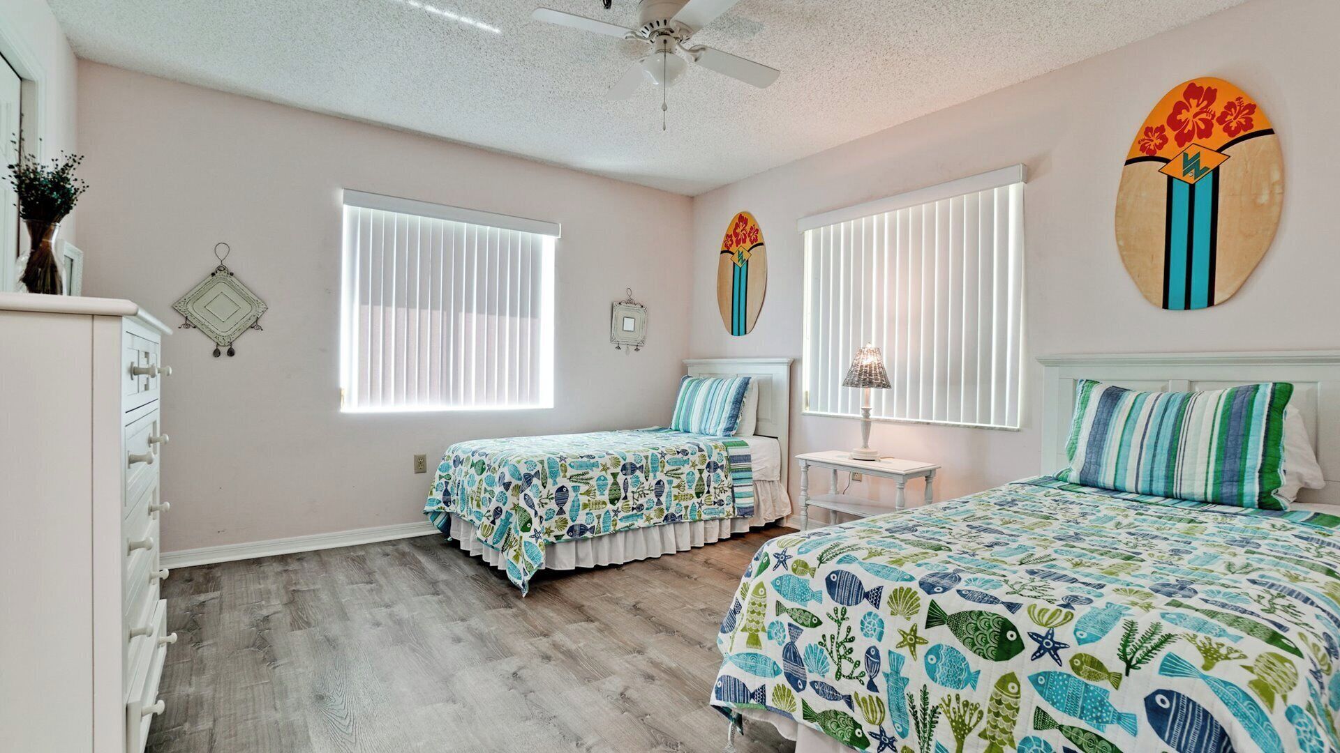 A bedroom with two beds, a ceiling fan, and a window with blinds.