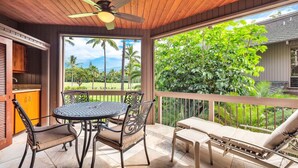 A covered patio with a table and chairs, a ceiling fan, and a view of lush greenery. - Lush View in Sunny Kona-Keauhou! Kitchen Ease, Lanai, Laundry, WiFi, TV Kanaloa 1204 (KAILUA-KONA)